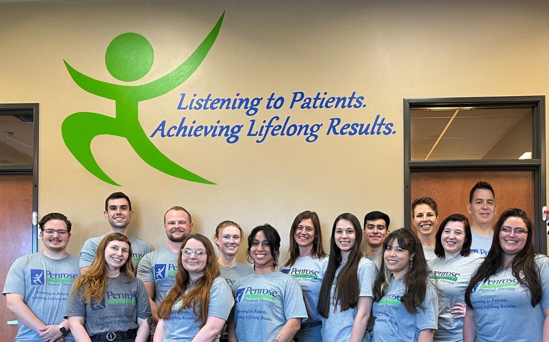 Penrose & Associates Physical Therapy staff standing for a group photo in front of a wall with the Penrose logo on it.