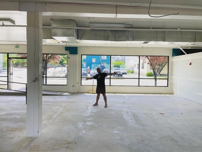 a man standing with his arms outstretched inside a big, empty retail space.