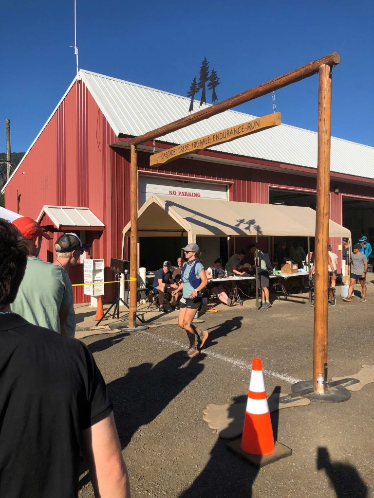 Hannah McLean crossing the finish line at the Cascade Crest 100 with a red building in the background