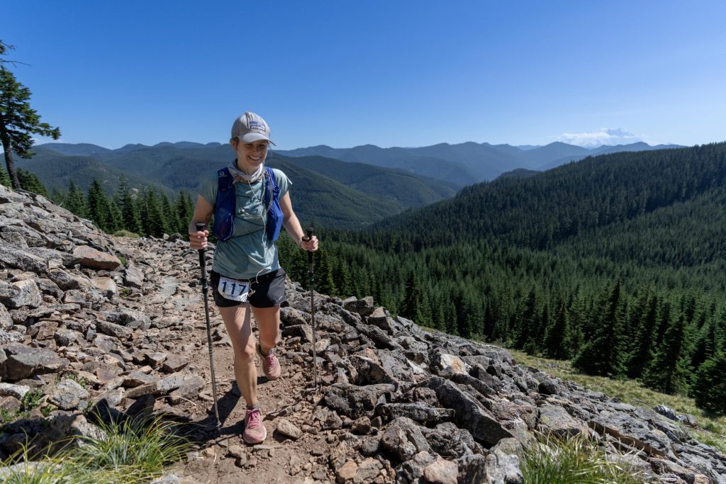 Hannah McLean running high on a mountain with two walking sticks in the Cascade Crest 100