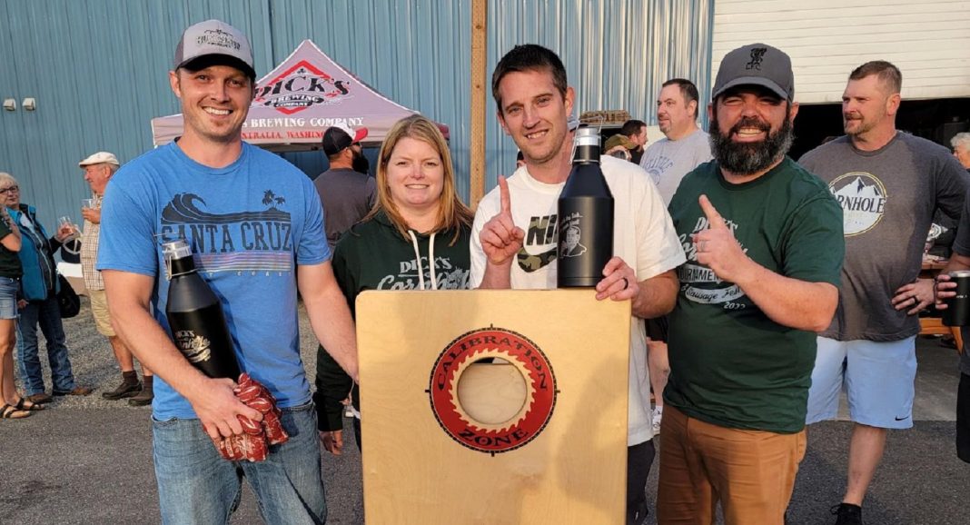 four people stand at a podium, smiling for the camera, two are holding growlers and two are holding up their index finger.
