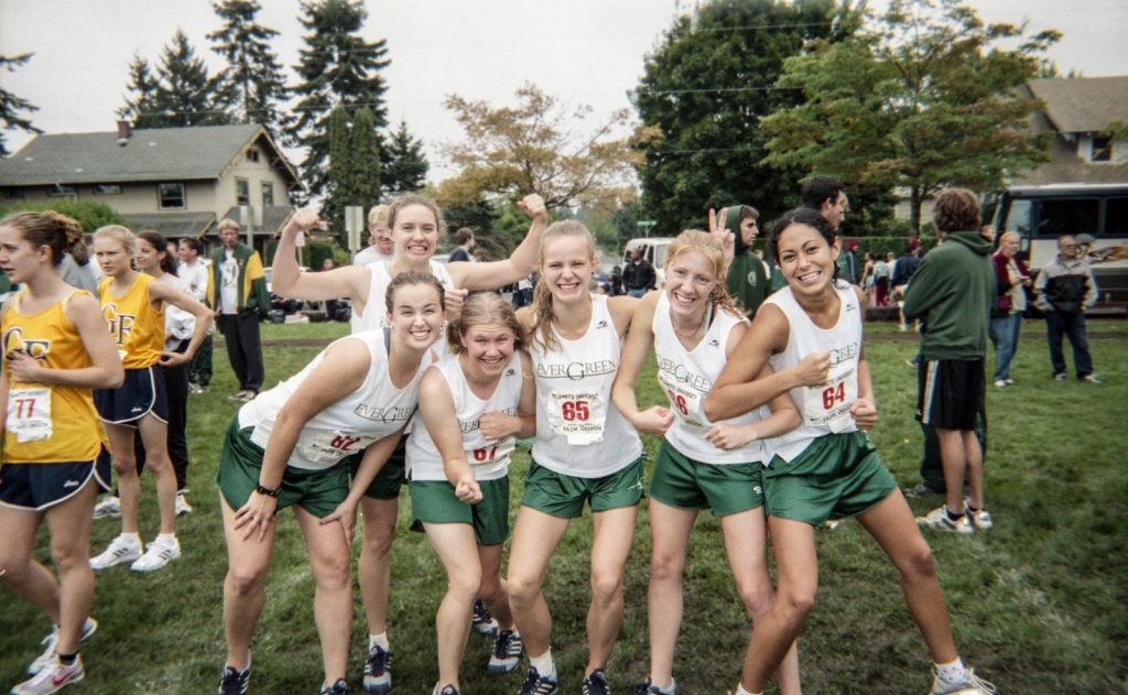 female runners in green shorts and white tank tops that say, 'Evergreen' pose for a photo.