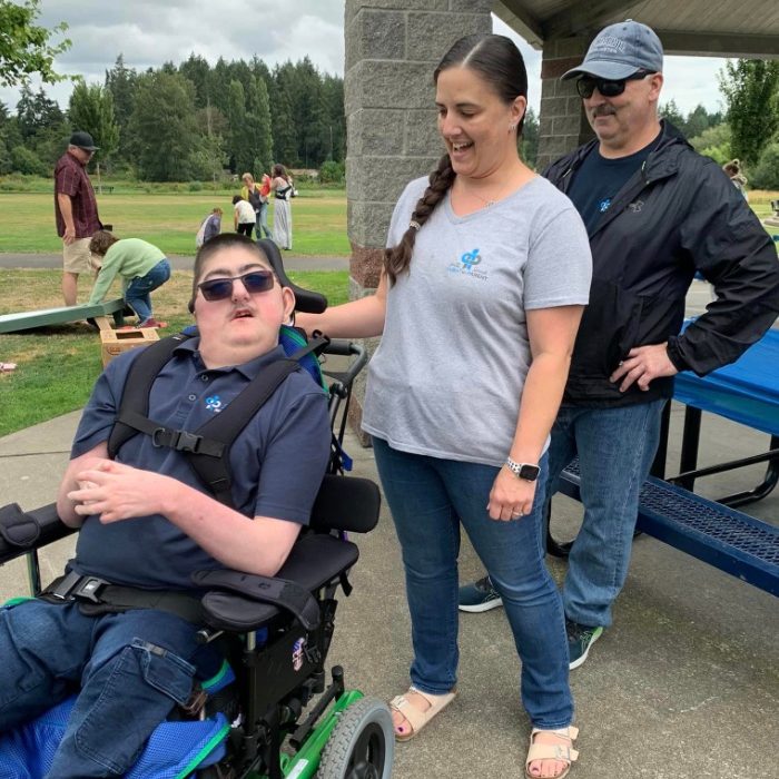 a couple stands behind a young man in a wheelchair in a park