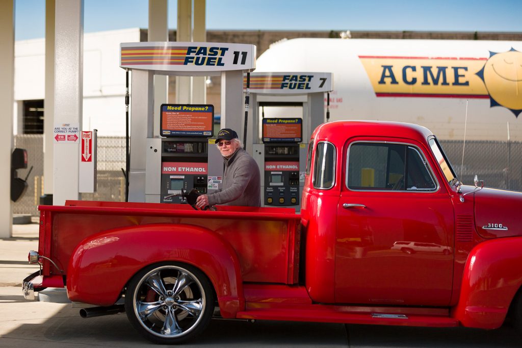 Classic red pick up truck with a man filling it with gas