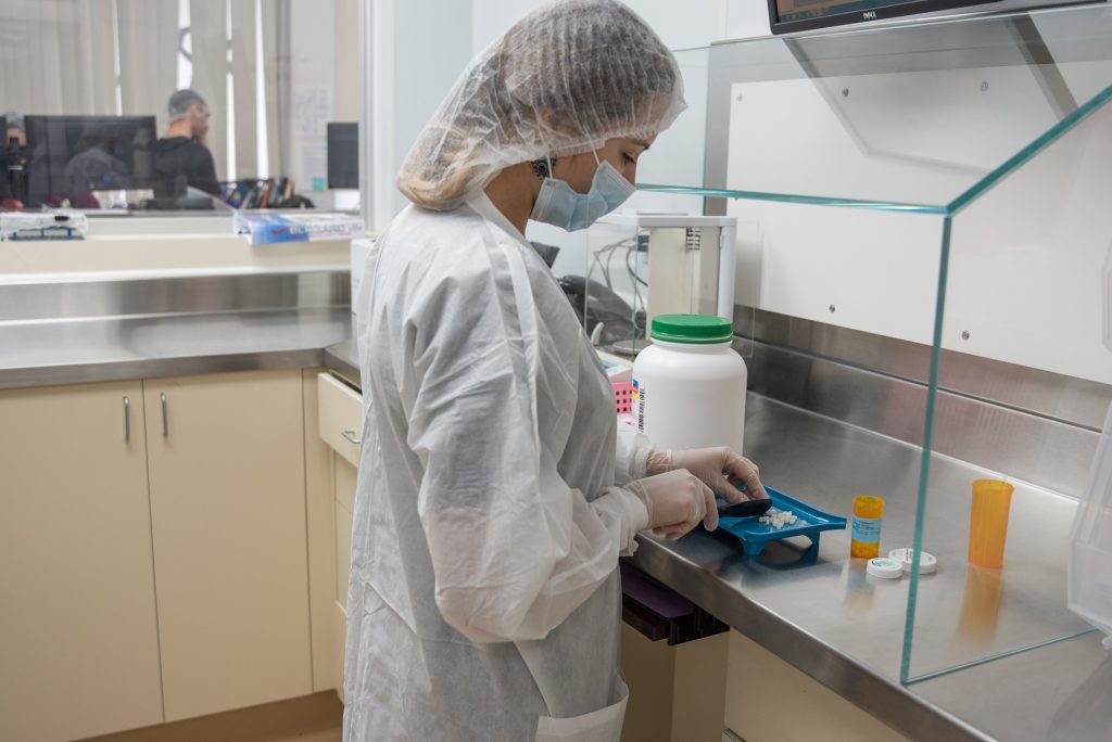 A person in scrubs, hair net and mask works on pills in a pharmacy