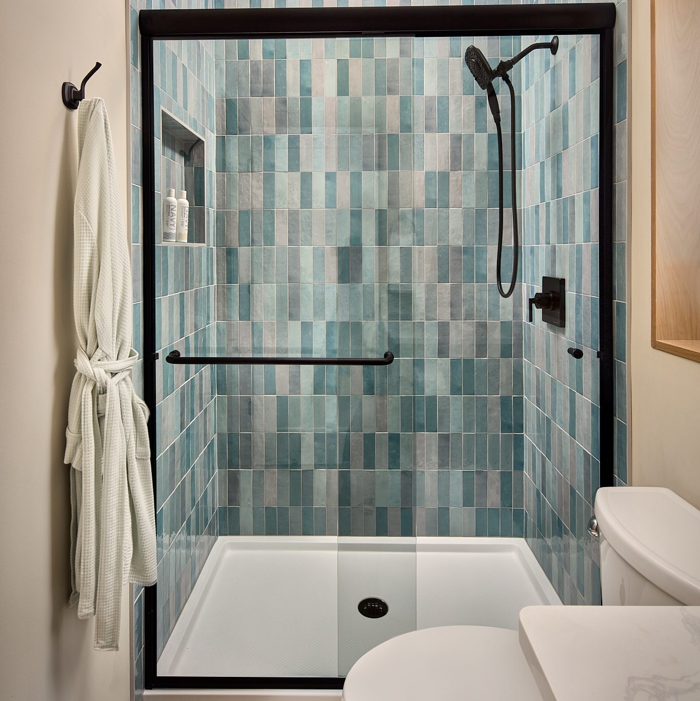 small bathroom with a single sink, toilet and a walk-in shower with blue-green and grey tiles going to the ceiling.