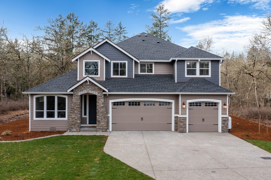 a brown, two-story home with white trim, a paved driveway and three car garage and a grass front yard