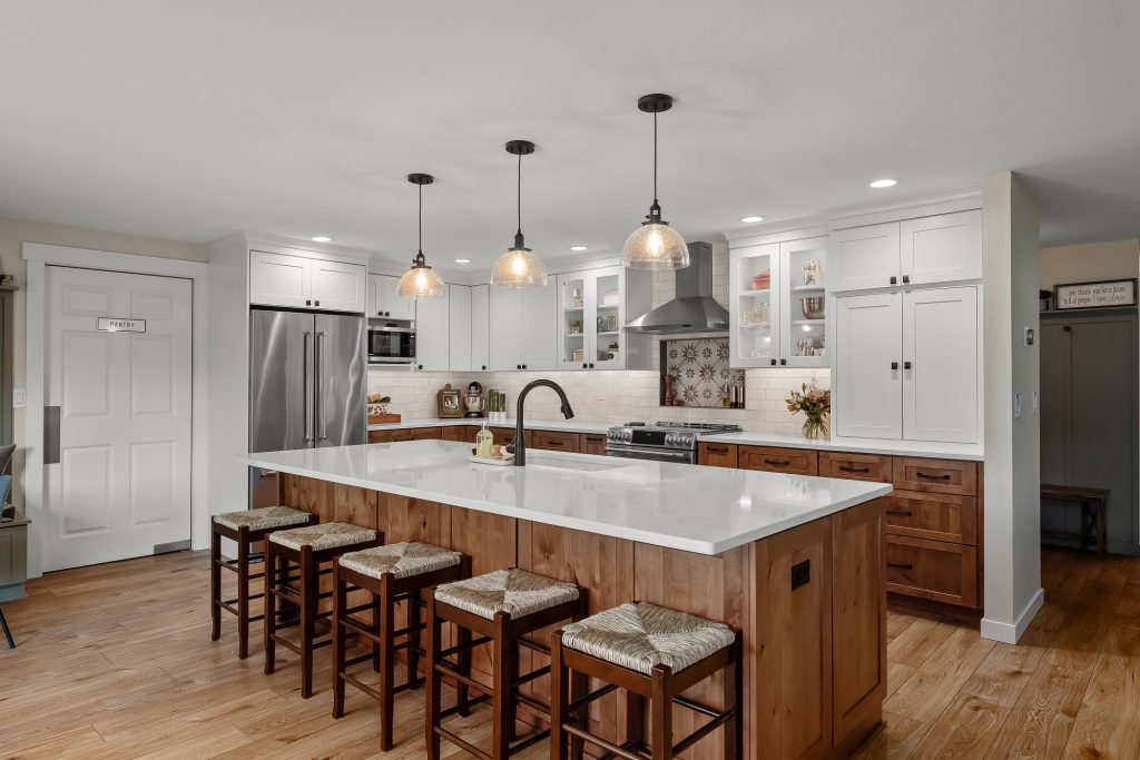 a kitchen with white cabinets, light wood island with a sink and five stools.