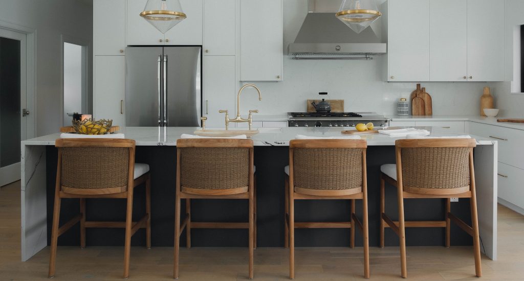 a kitchen with tall chairs at an island, featuring white cabinets and gold kitchen sink faucet.