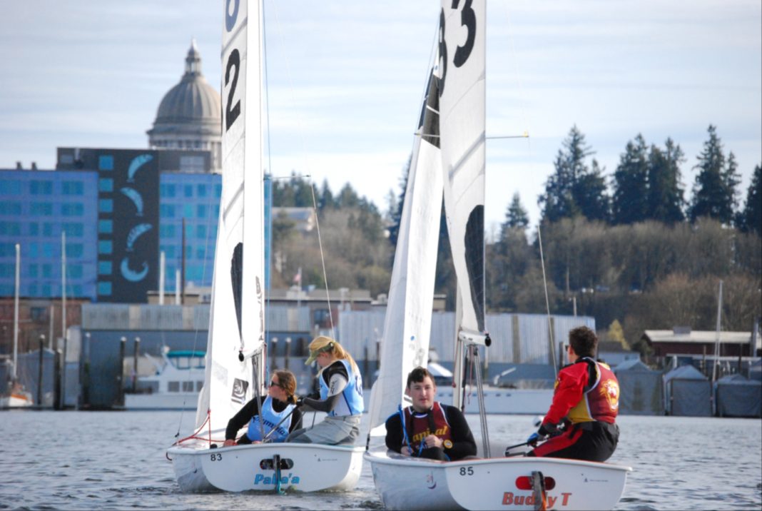 Two sail boats, each with two people in them, with the Olympia capital building behind it.