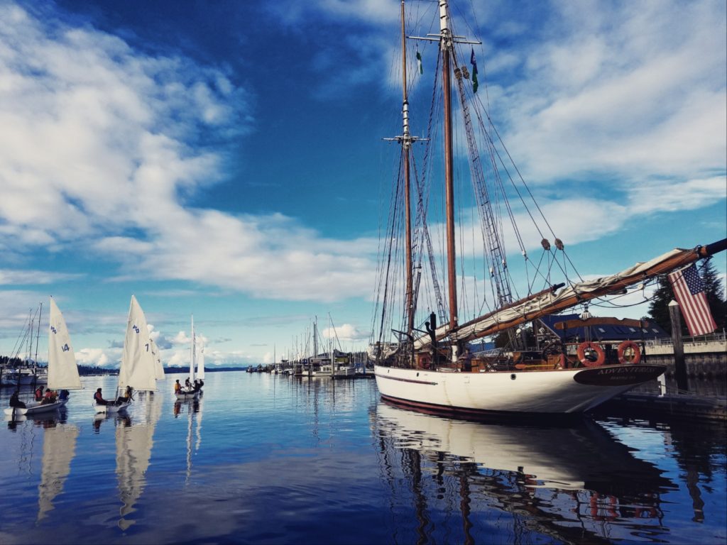 100-year-old vintage schooner sites at a dock with three sailboats full of people sail by.