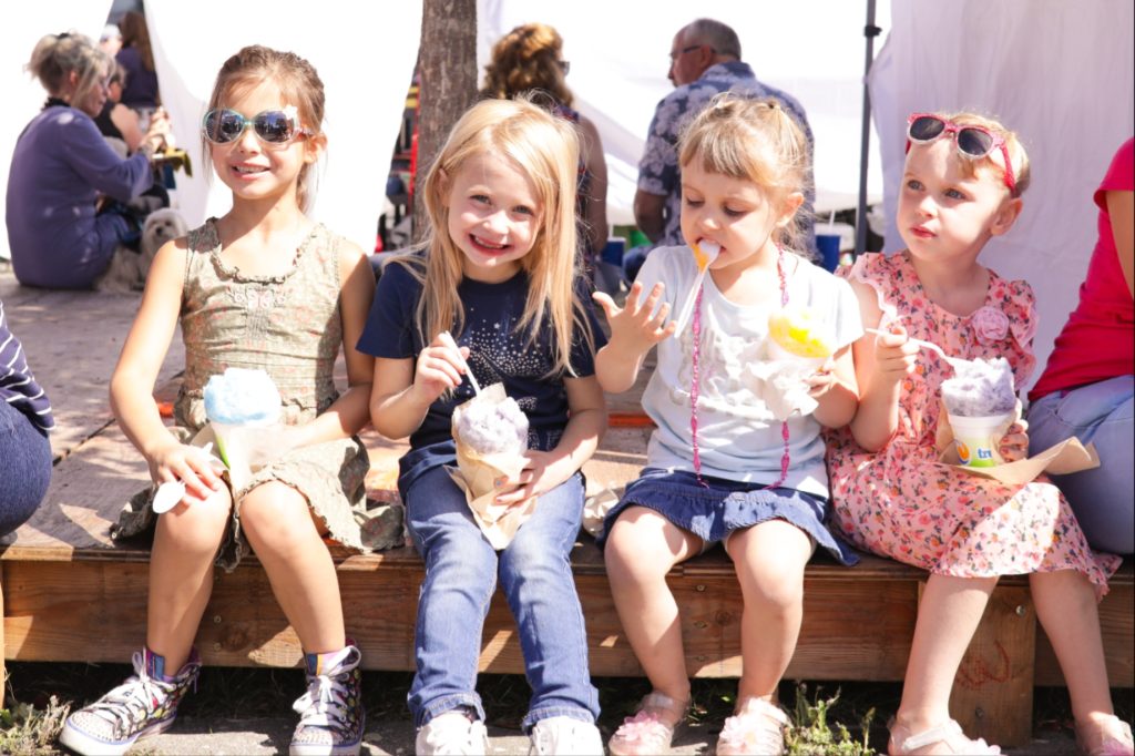 four kids sit on a wood platform eating sno cones