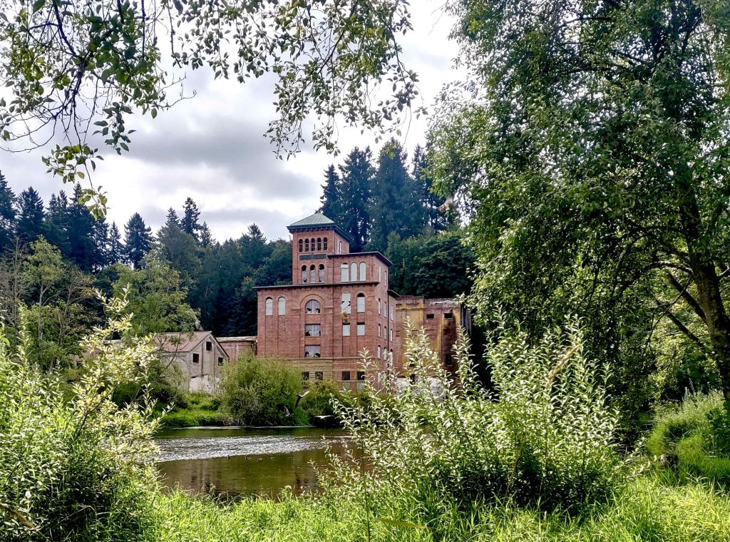 Tall brick building jutting out in front of trees and bushes with the Deschutes River in front