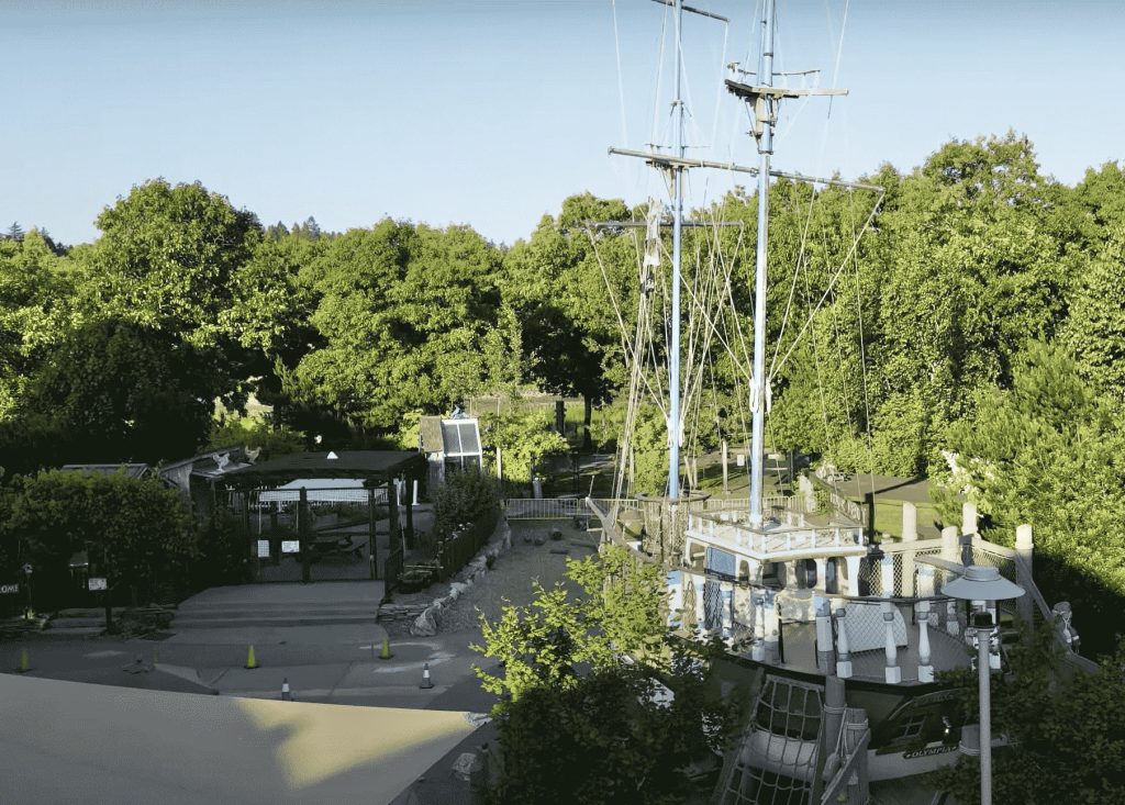 concrete outdoor space with trees all around and a ship with tall masts next to it