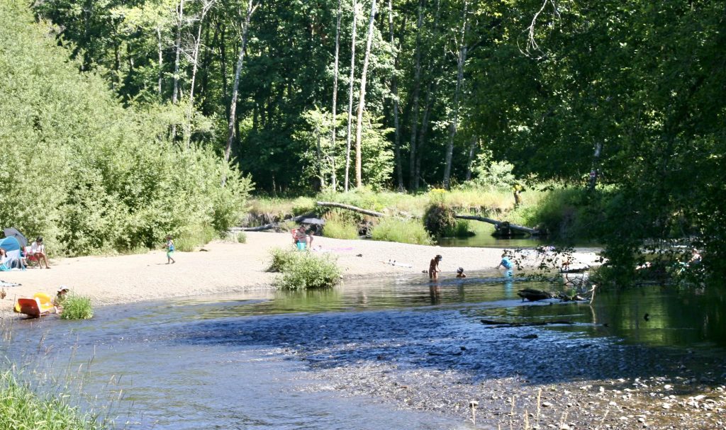 Deschutes river with kids and adults in the water and on the beach. Some with chairs or floaties