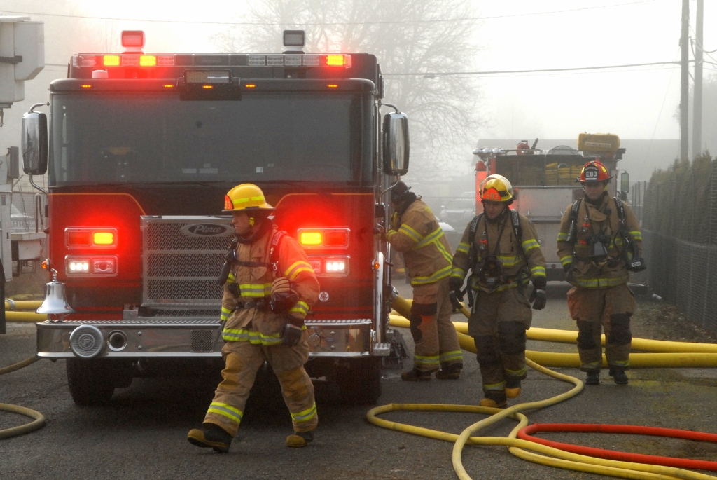 firemen walking around a fire truck, enveloped in smoke