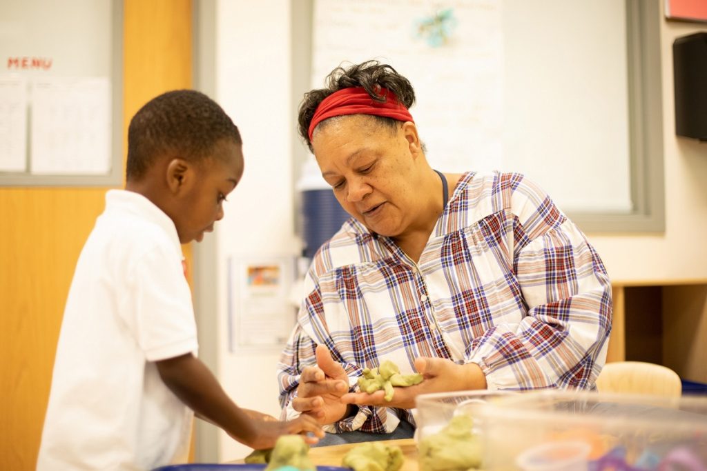 Darlene Mate sitting at a table with a young student standing next to her. They are working with clay