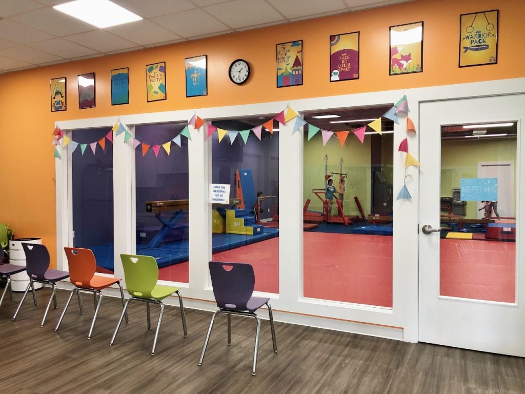 orange, green, and purple chairs lined up in a room with glass panels and and a door looking into gym area at The Little Gym