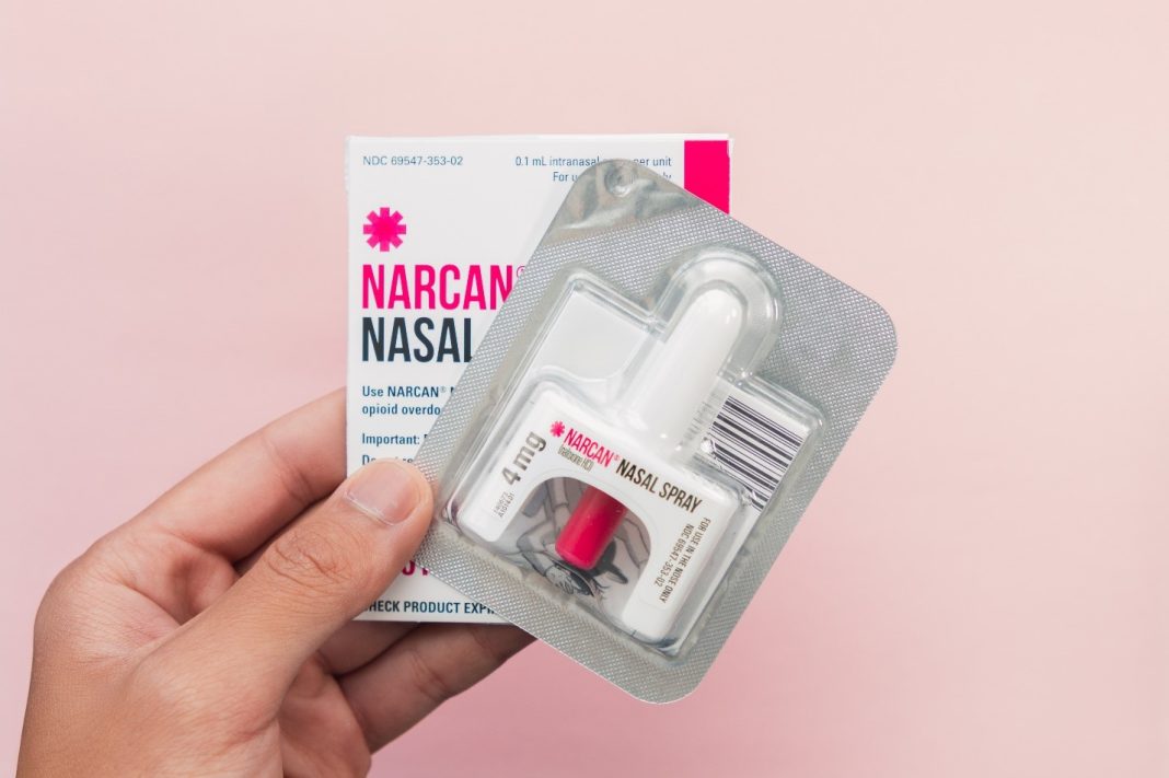 Nasal Spray Narcan in a hand on a pink gradient background