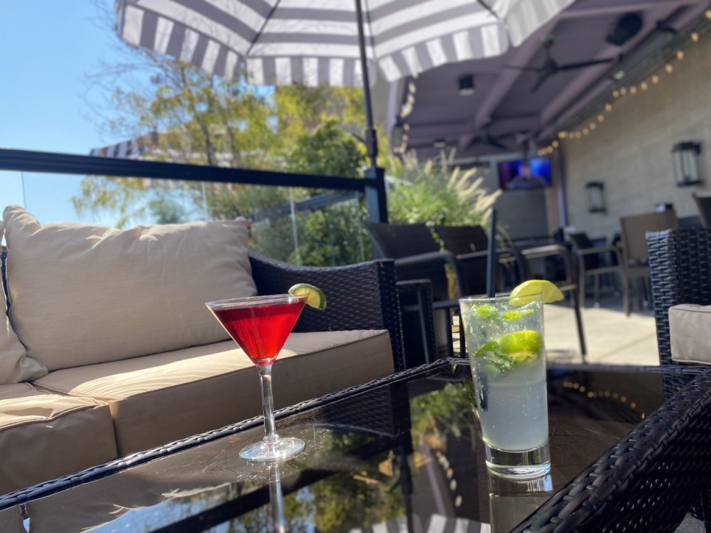 patio with umbrellas, outdoor lawn furniture including a couch and chairs, with a cocktail on a low table