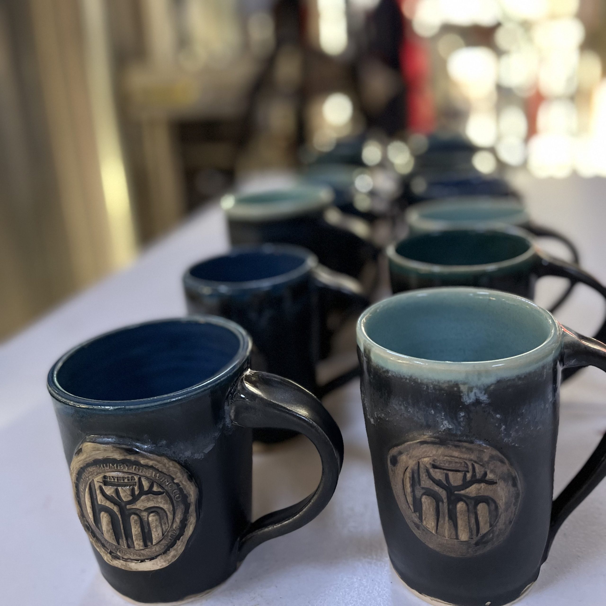 Rows of Headless Mumby Brewing ceramic mugs on a counter.