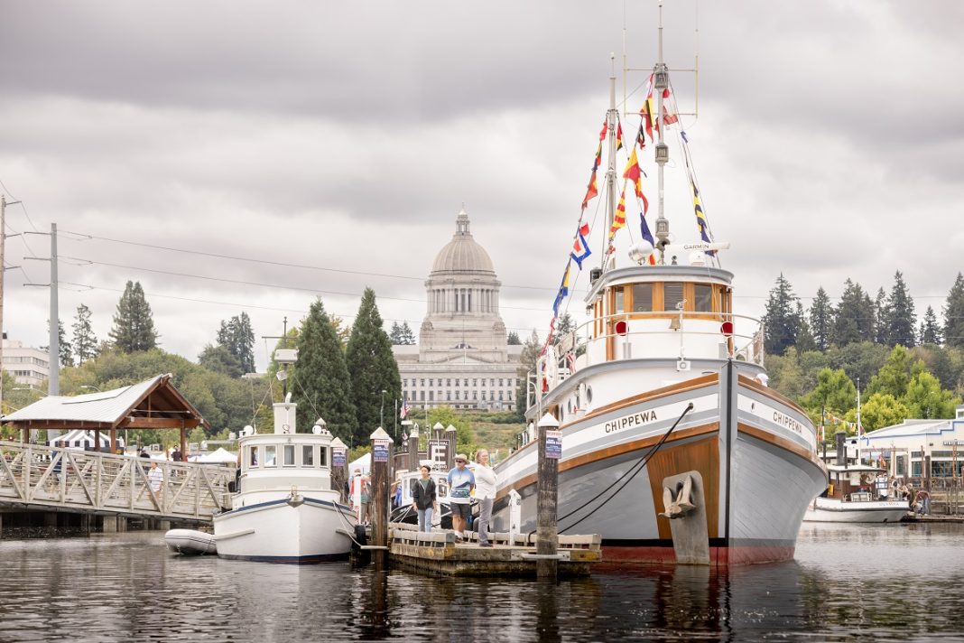 tugboats by a dock with people standing around them and the Olympia capital building in the background.