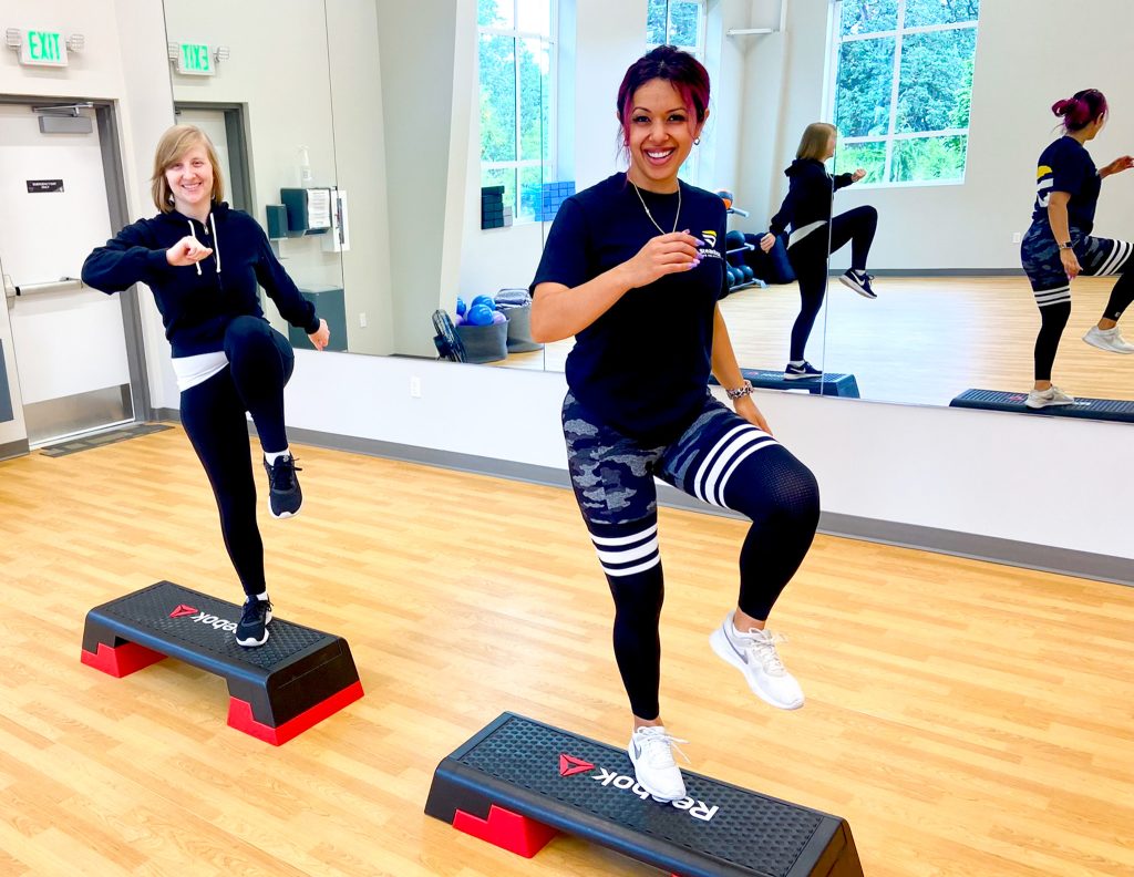 Two women in front of large mirror working out on step ups.
