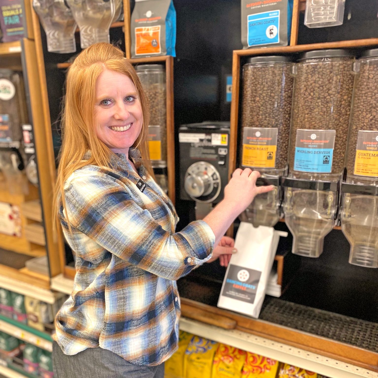 a woman in a grocery store puts fresh coffee from a depenser into a bag.