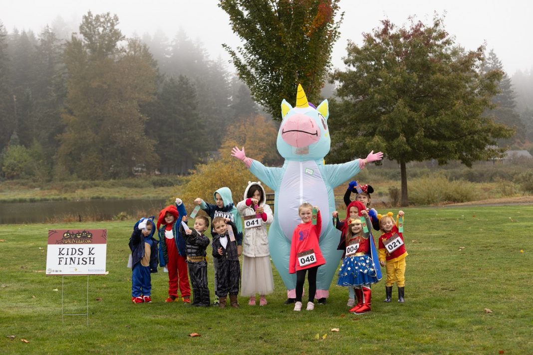 A bunch of kids pose with a person in a blow-up unicorn halloween costume on the grass after the All Kids Win Haunted 4K