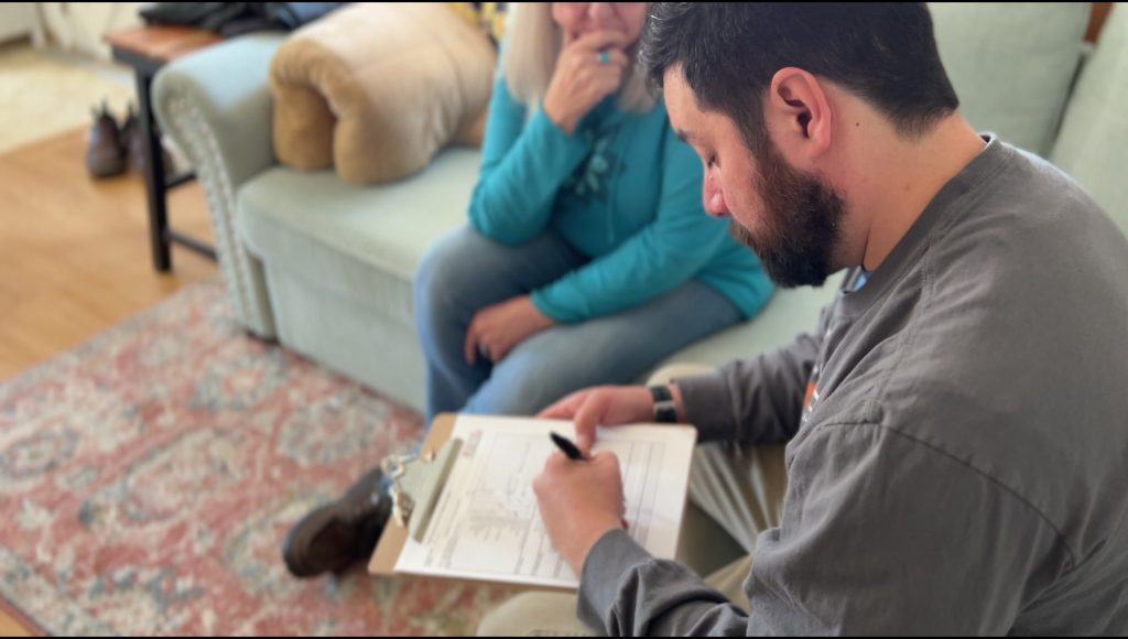 Manny Owens sitting with a homeowner going over a list on a clipboard