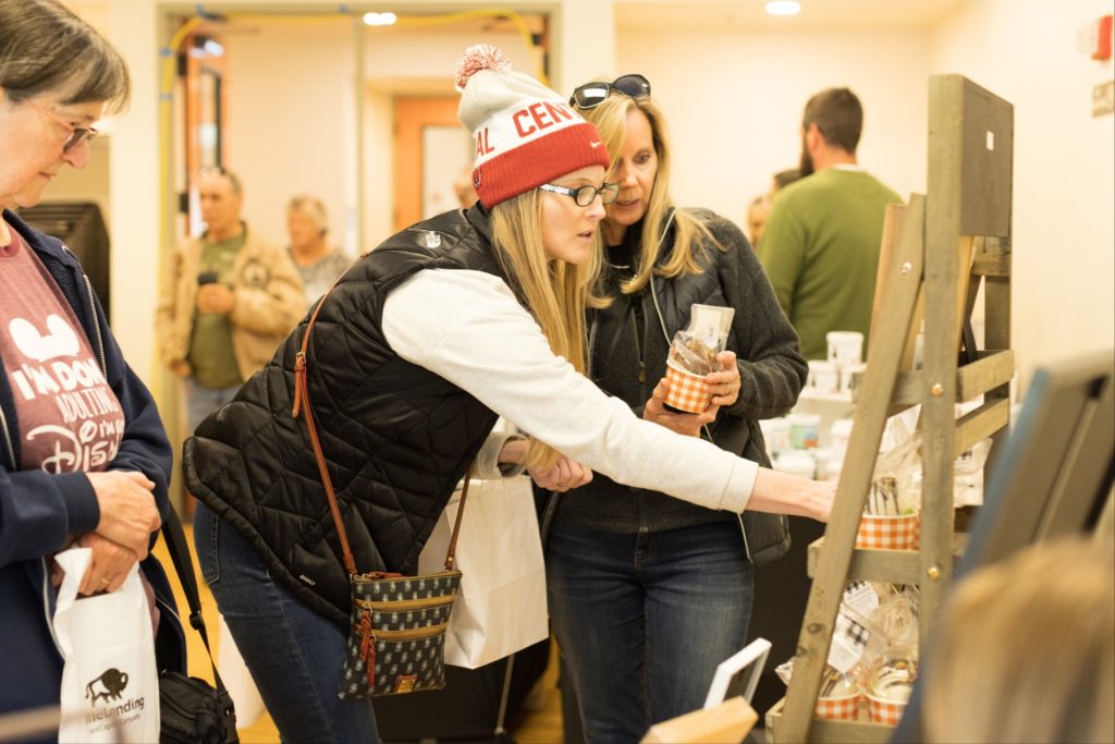 Women looking at products in paper cups on a wooden shelf.