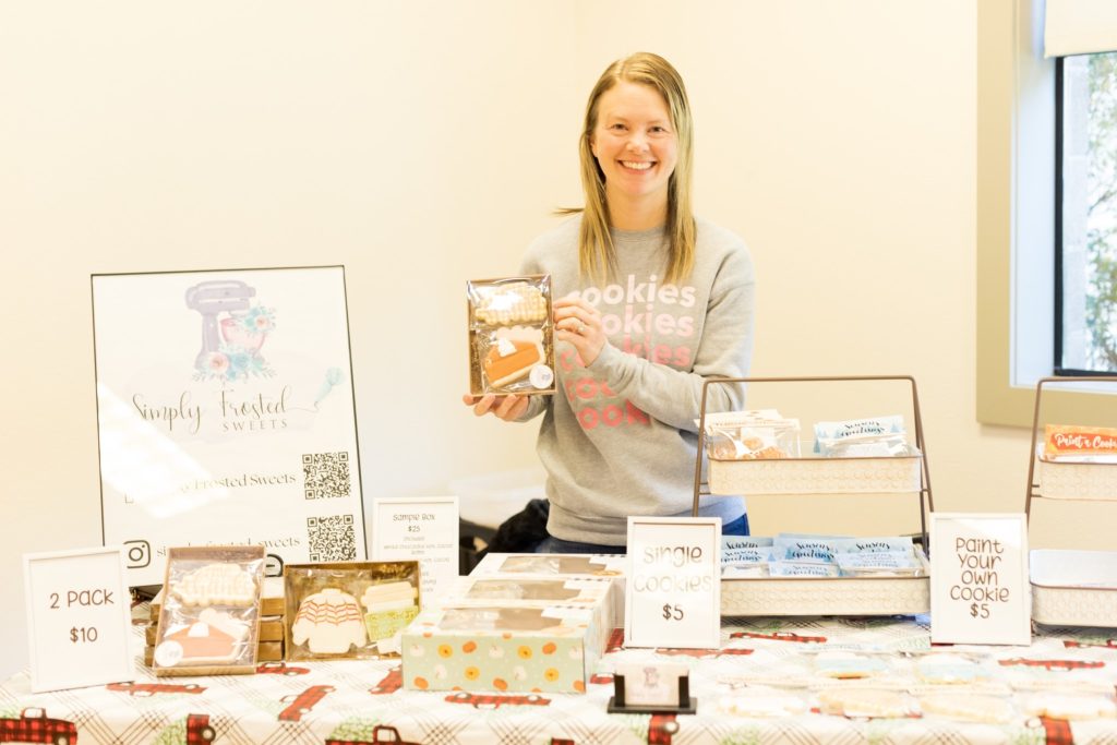 women holds up a box of cookies behind her table that is covered in boxes of cookies and price signs