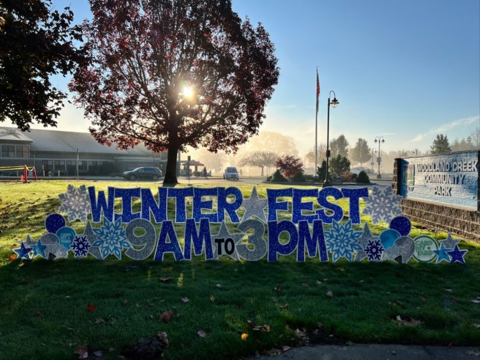 Silver and blue sign that says, 'Winter Fest 9 am to 3 pm' in a grass lawn.