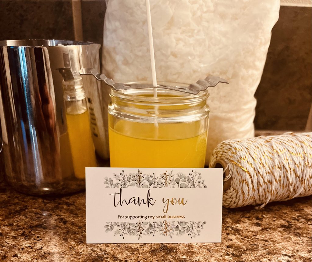 a soy based candle in a glass jar with a long wick and a business card in front of it that says, 'Thank you for supporting my small business.'