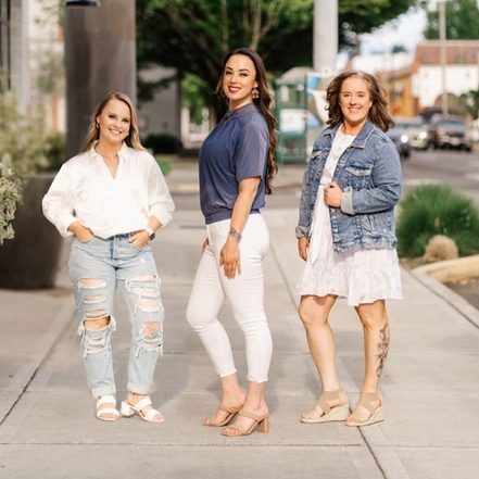 Three woman pose for a photo outside on a sidewalk. 