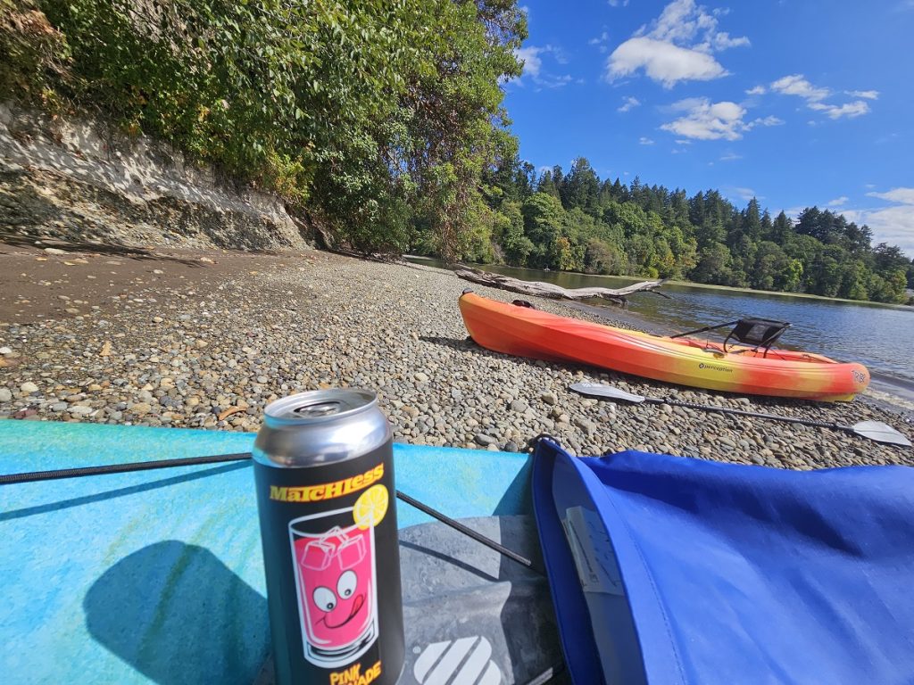 kayaks on the shore of Squaxin Park with a Matchless Brewing can