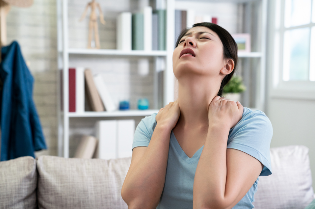 women sitting on a couch with her hands on her neck and her head raised up with a pained expression