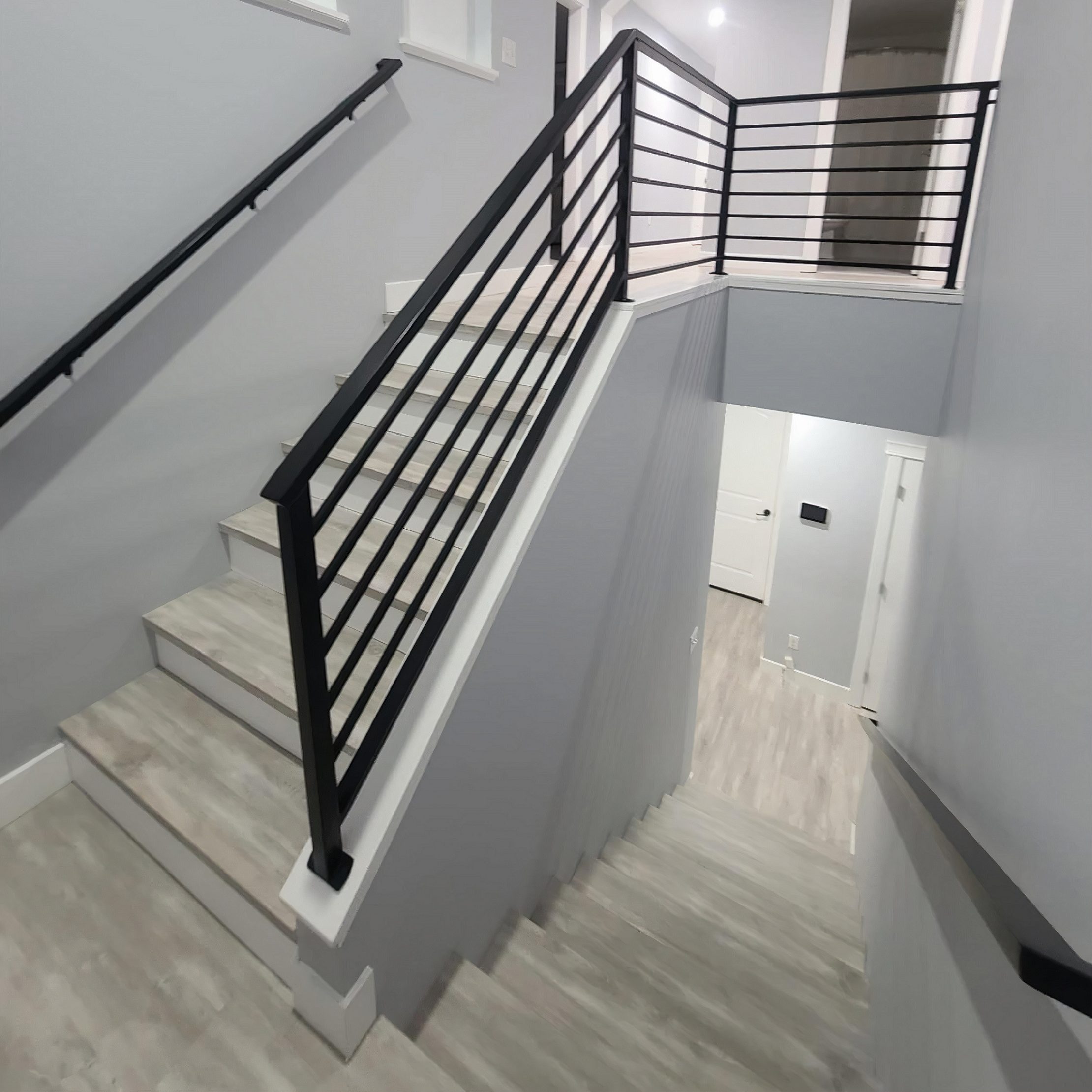 stairs in a home with a black metal banister and a light-colored, wood-look laminate flooring