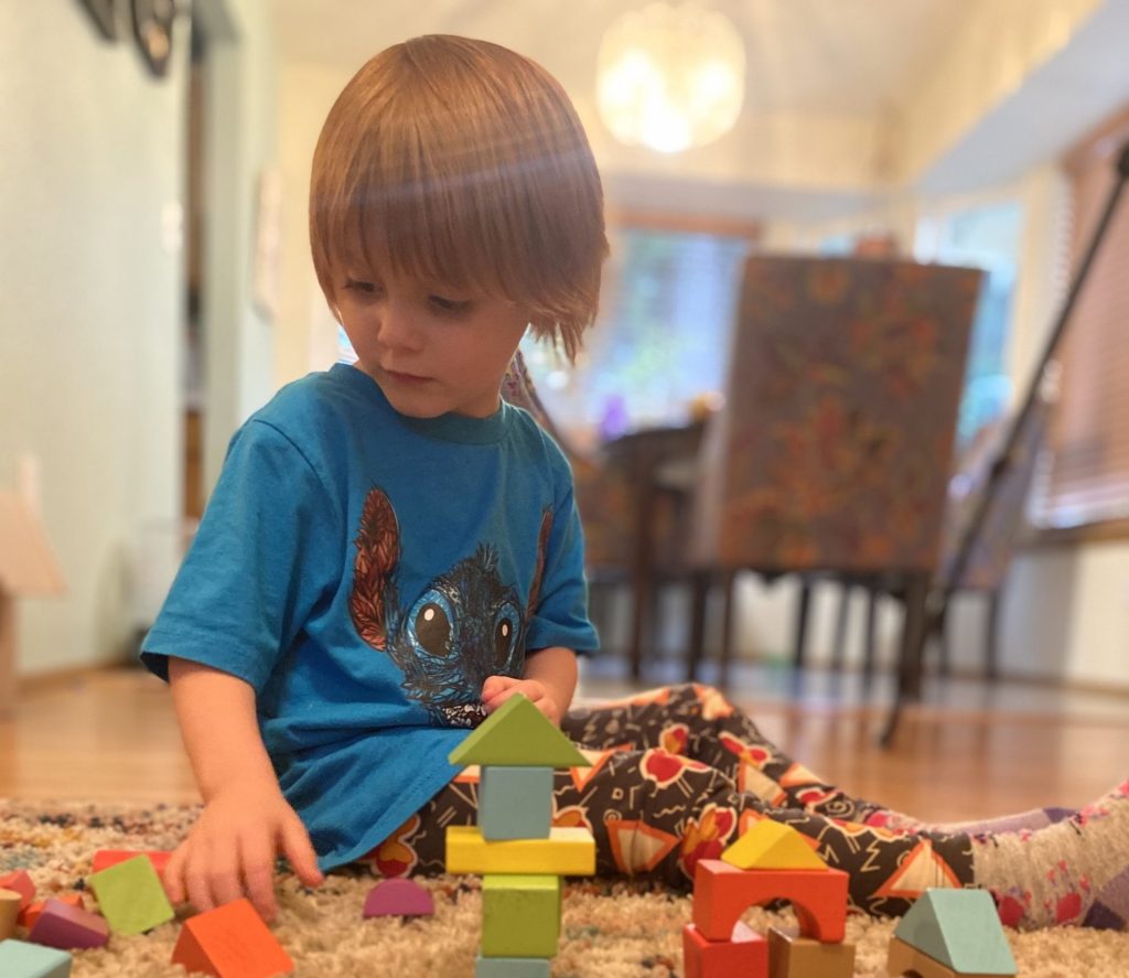 child sitting on the floor in a house playing with wood blocks