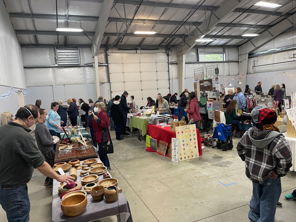 large groups of people mill around arts and their tables full of goodd in a large warehouse