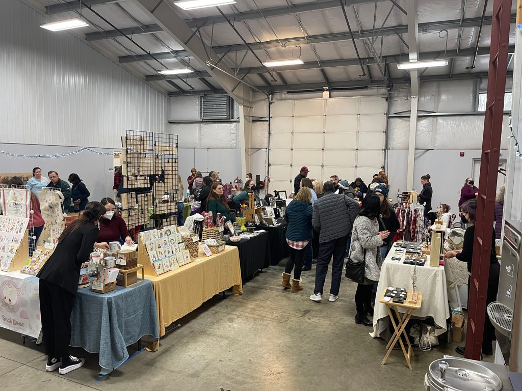 large groups of people mill around arts and their tables full of goodd in a large warehouse