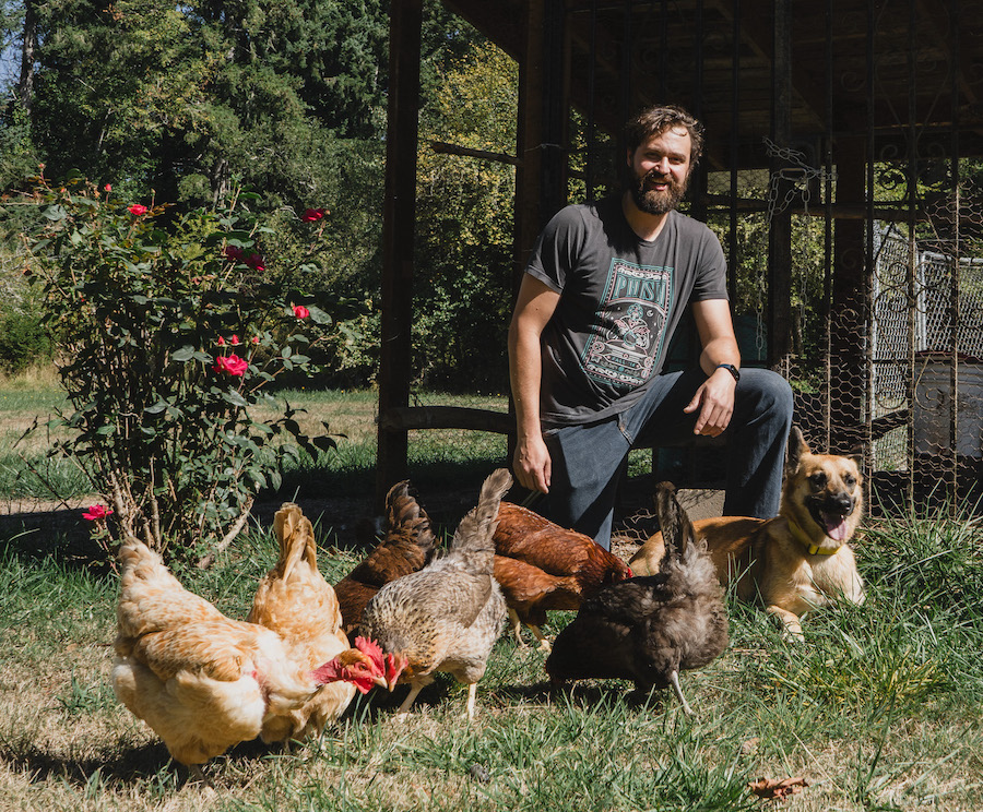 Chris VanderPluym, owner of VP Acupuncture, on one knee with a flock of chickens