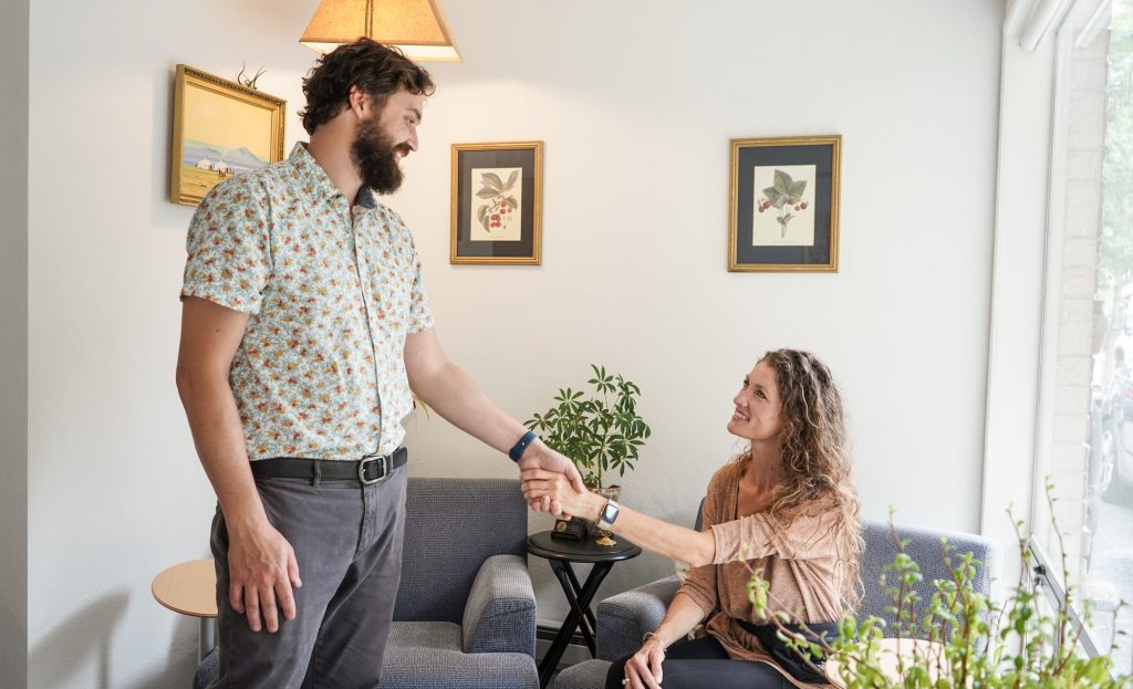 Chris VanderPluym, owner of VP Acupuncture, standing and shaking hands with a woman who is sitting in a chair