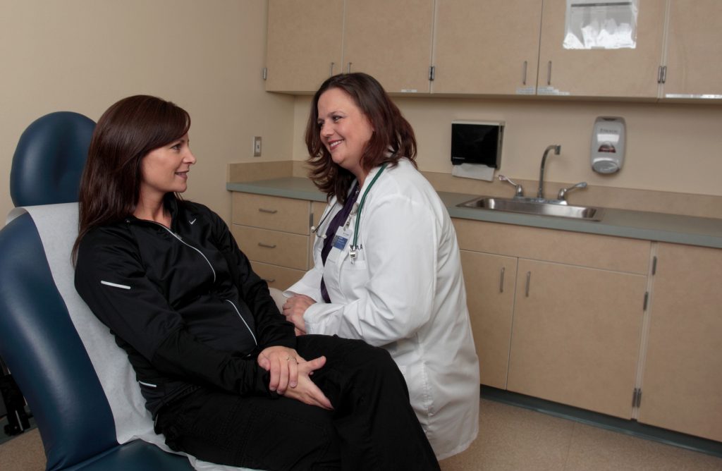 A women in an exam room chair talking to a woman doctor