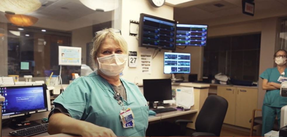 a nurse in green scrubs with a mask on sitting at a desk