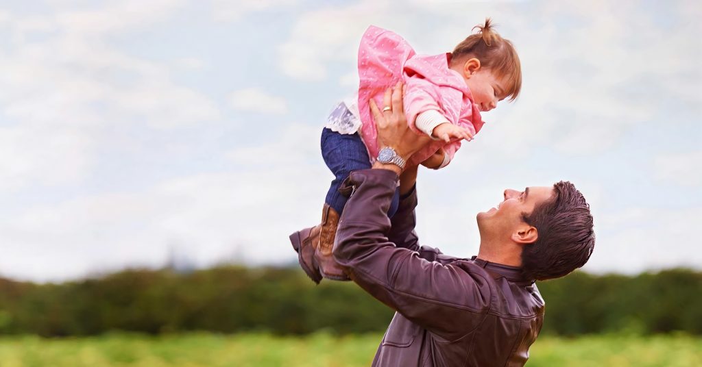 Man holding a toddler up in his arms with a field in the background