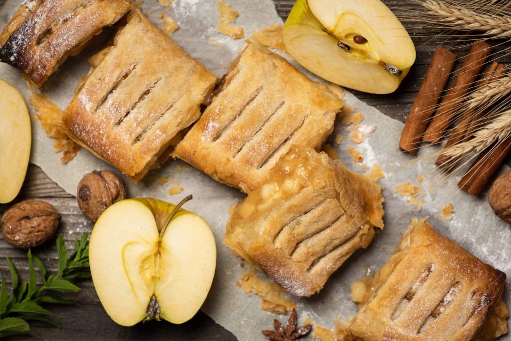 Slices of freshly baked homemade pie with apples, walnuts and cinnamon. On baking paper and a wooden table