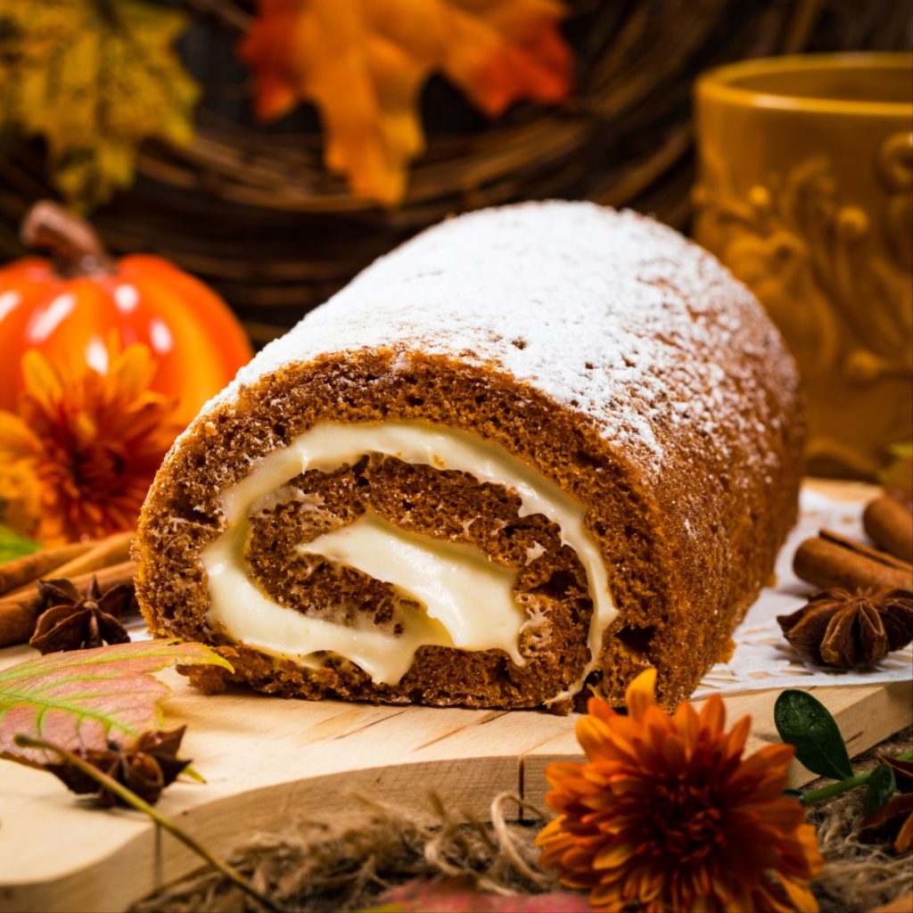 holiday chocolate log roll on a cutting board surrounded by fake fall foliage and pumpkins