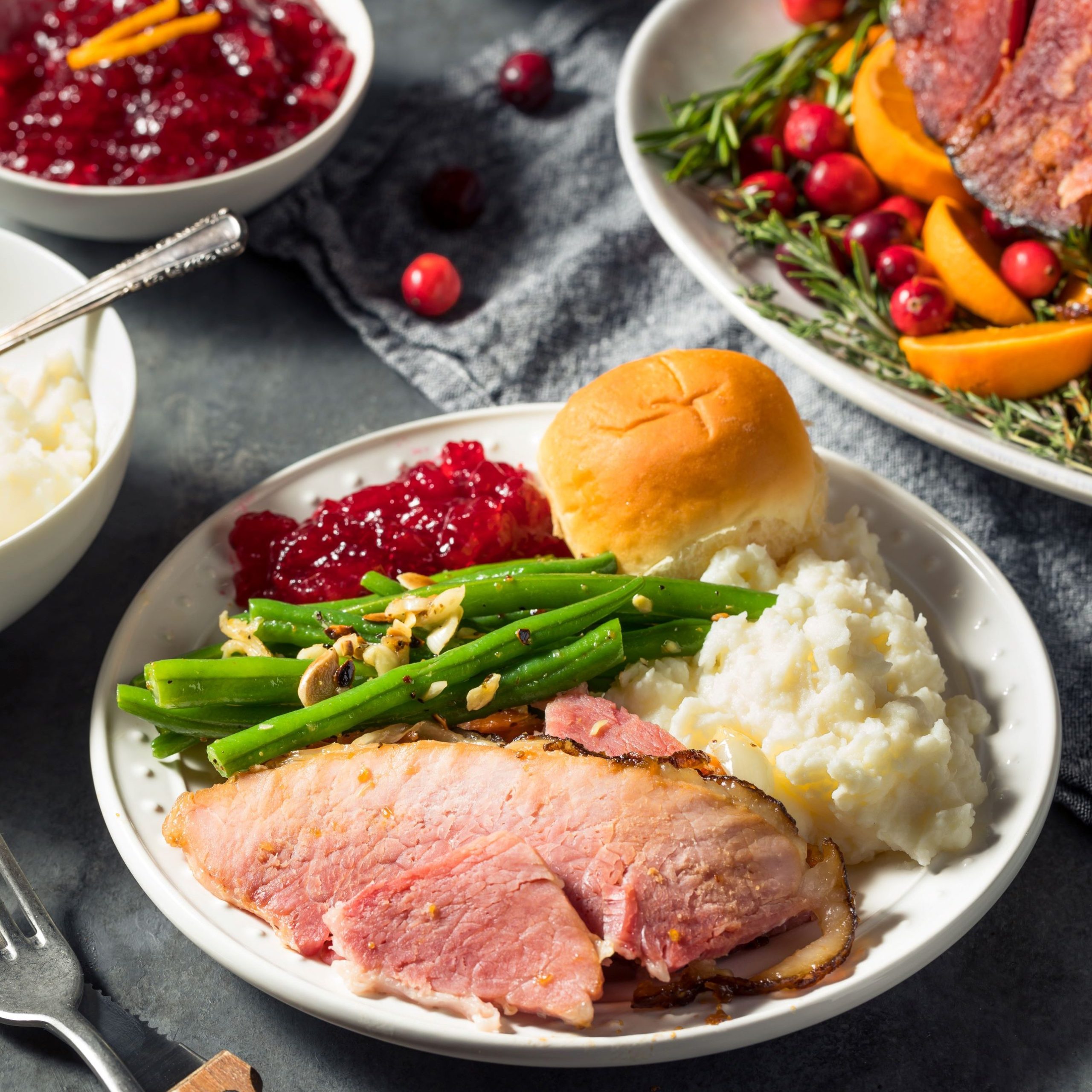 a table with plates full of traditional Thanksgiving dinner food items, rolls, mashed potatoes, turkey, cranberry sauce and green beans