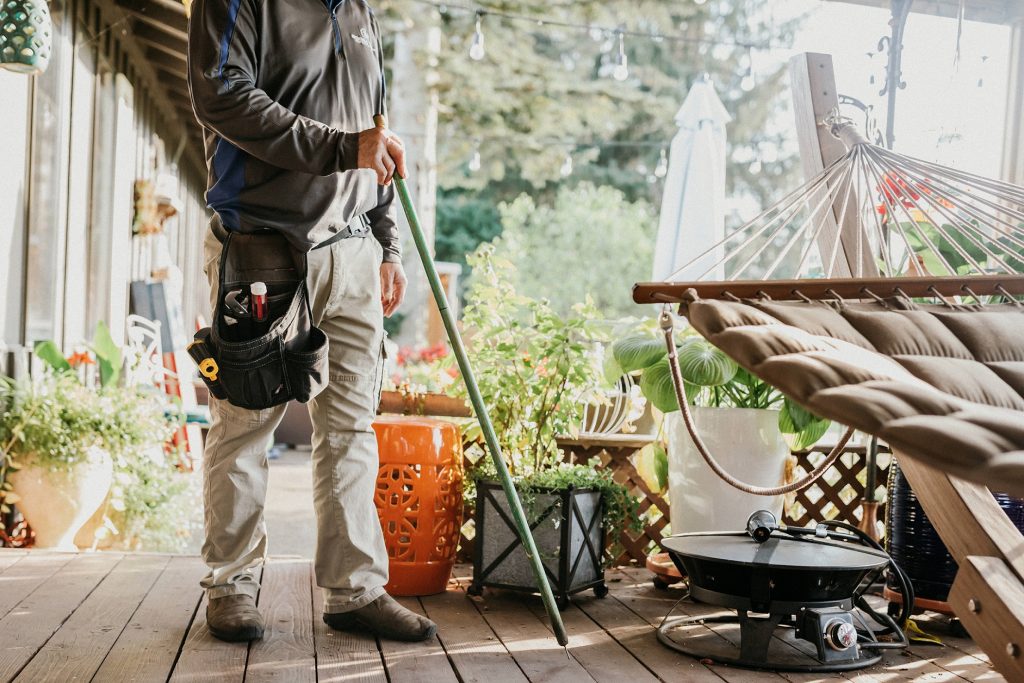 Boggs Inspection Services technician on a deck with a wooden pole in his hand and tool belt on his waist. He is standing next to a hammock